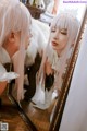 A woman with long white hair looking at herself in a mirror.