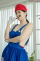 A woman in a blue dress and a red hat holding a spoon.