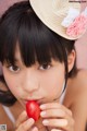 A young woman holding a cherry in front of her mouth.