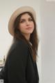 A woman wearing a hat standing in front of a wall.